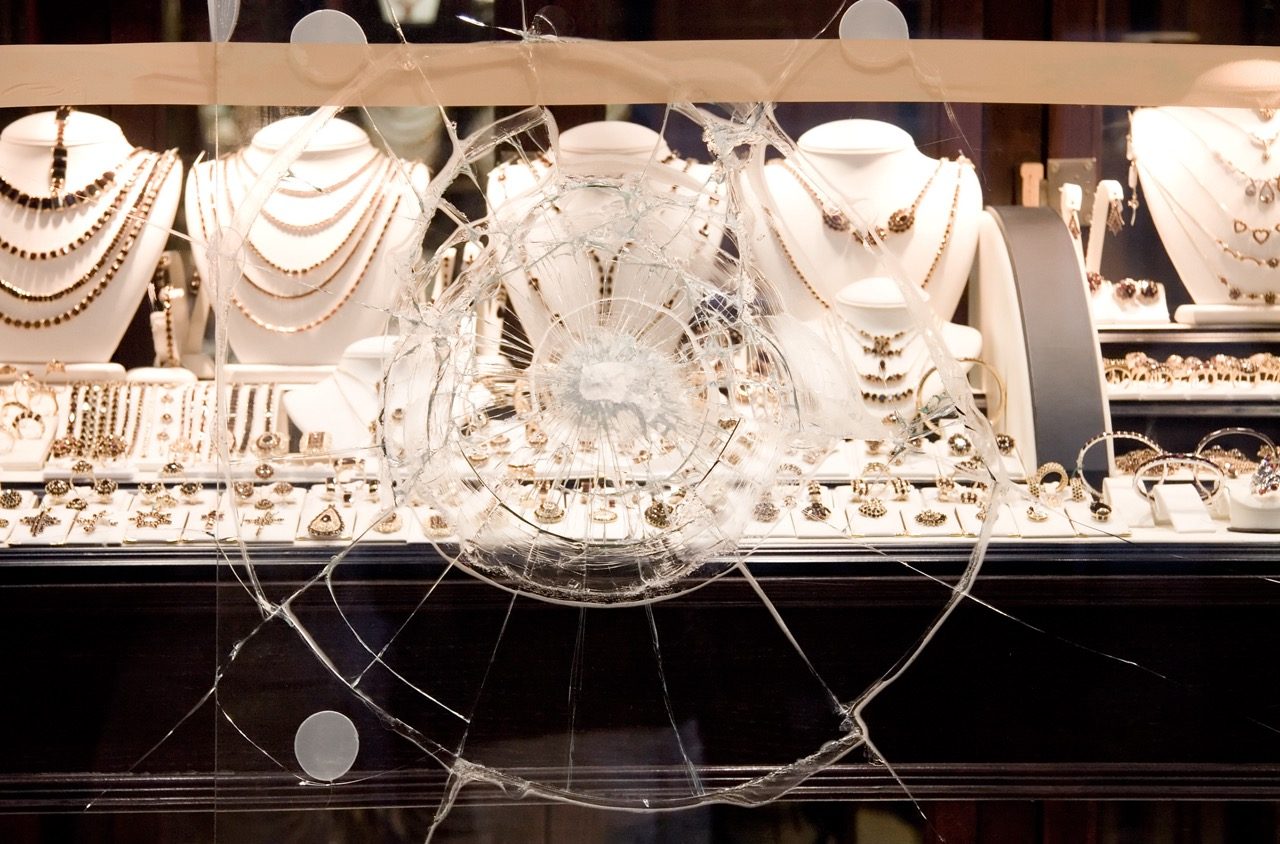 A display window struck hard enough to craze the glass in a wide spiderweb pattern. The pane is still in its frame, and the jewellery on the stands behind it is untouched.