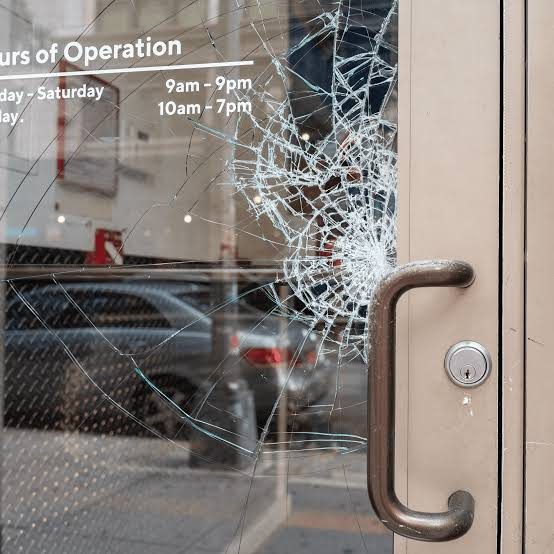 A glass shop door with an opening punched clean through it, ringed by radiating cracks, beside the door handle and lock.